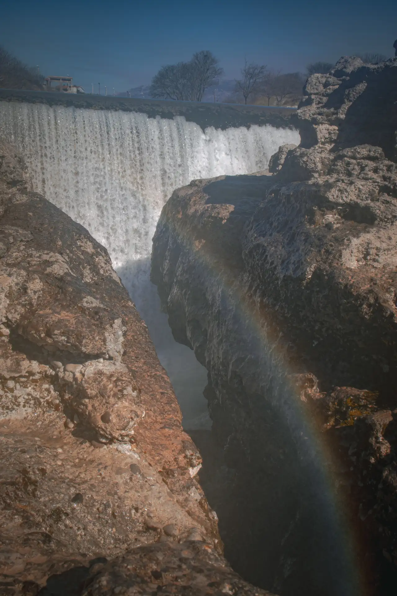 a waterfall over rocks with a rainbow