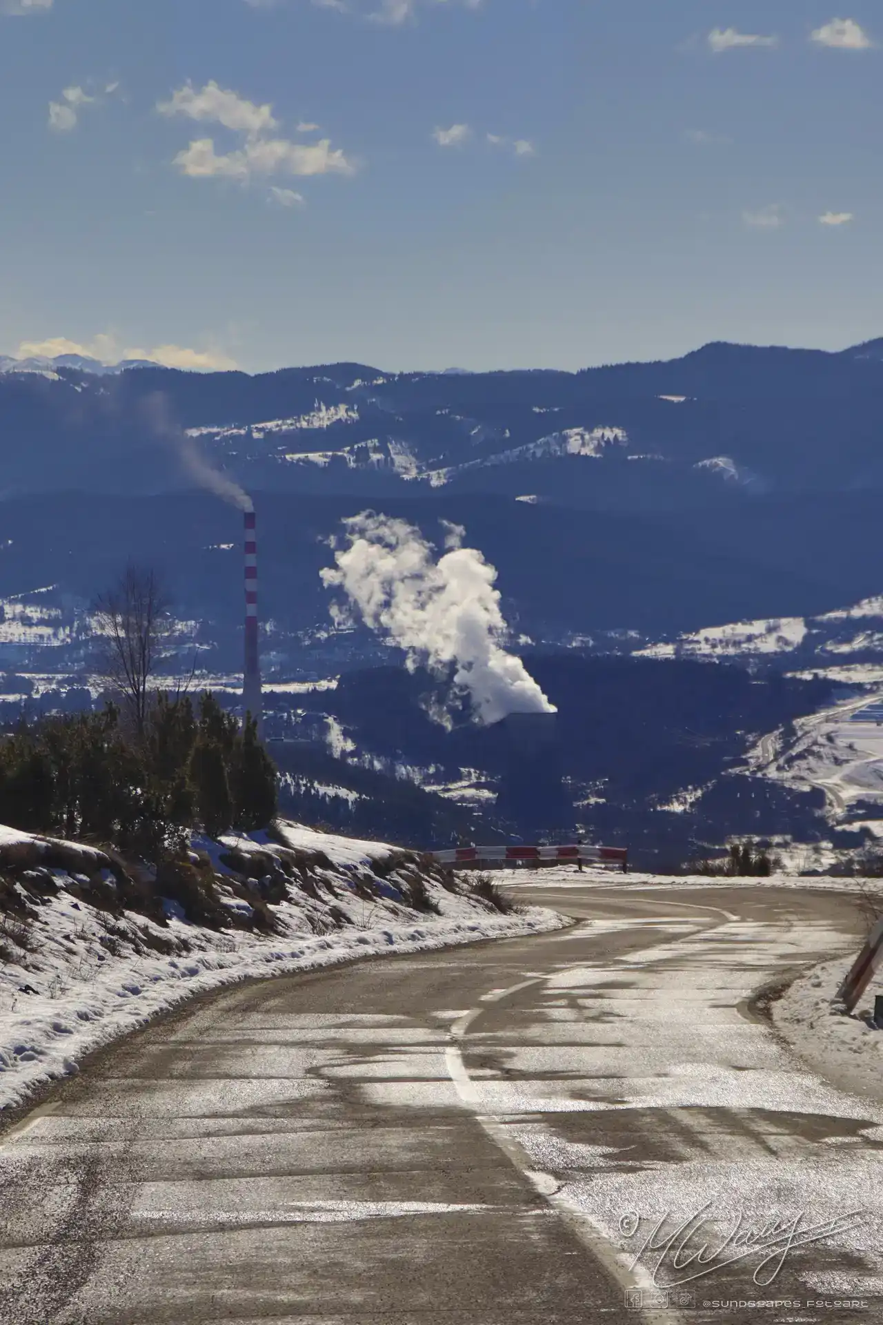 a road with smokestacks and mountains in the background