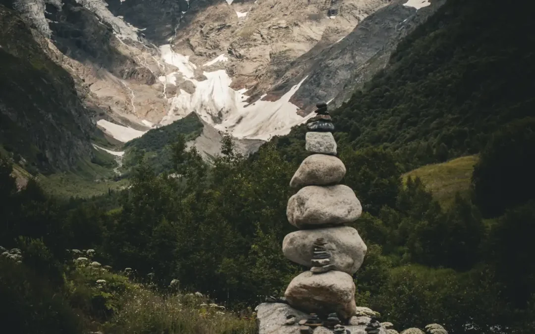 aufeinander geschichtete Steine vor einem Tal in Georgien. Berge mit Schneefeldern und der blaue Himmel im Hintergrund. Stressabbau durch das Betrachten.