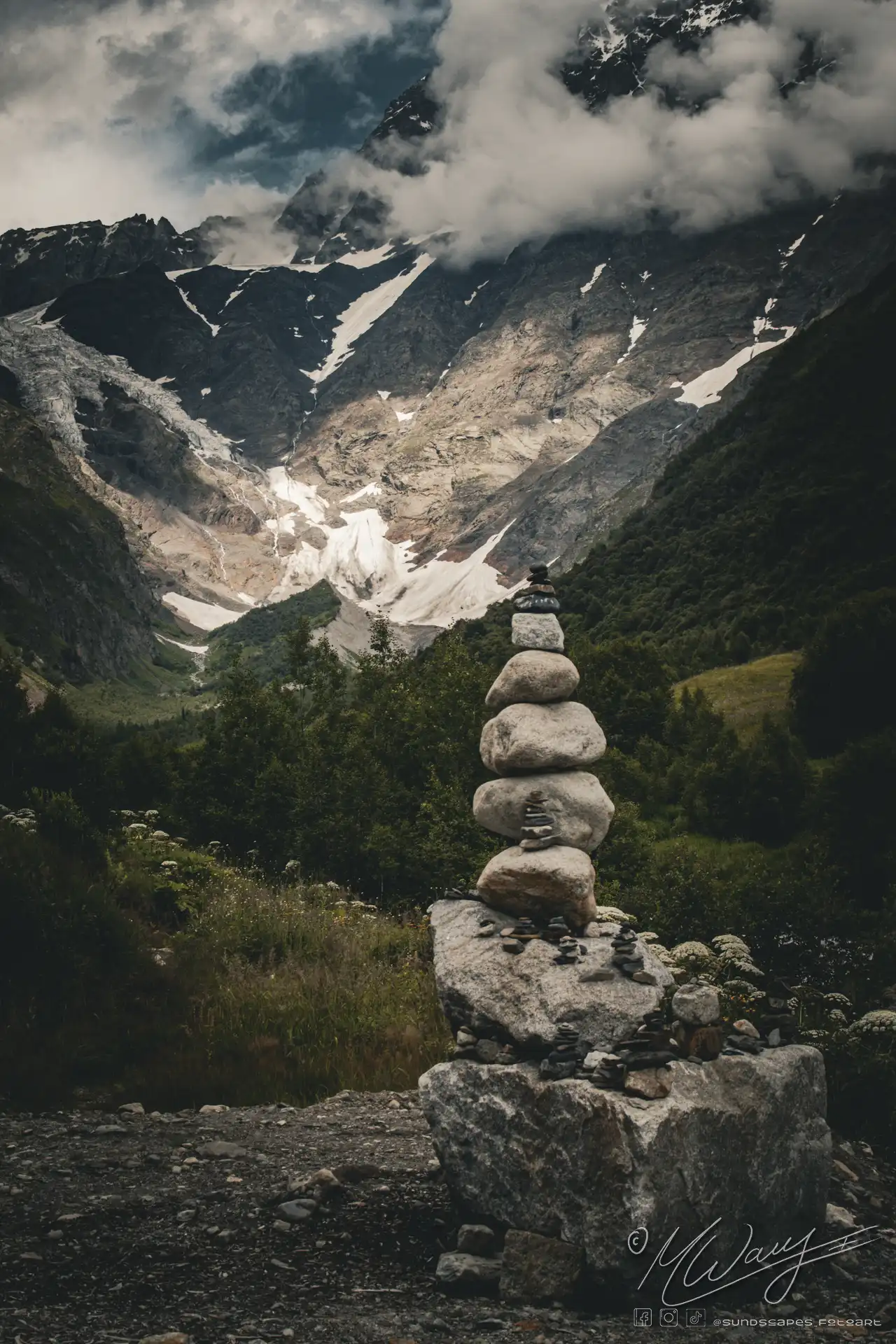 aufeinander geschichtete Steine vor einem Tal in Georgien. Berge mit Schneefeldern und der blaue Himmel im Hintergrund. Stressabbau durch das Betrachten.