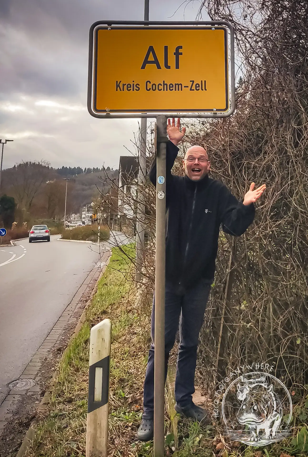 Ortschild "Alf" im Kreis Cochem-Zell / Moseltal. Micha steht daneben und winkt.