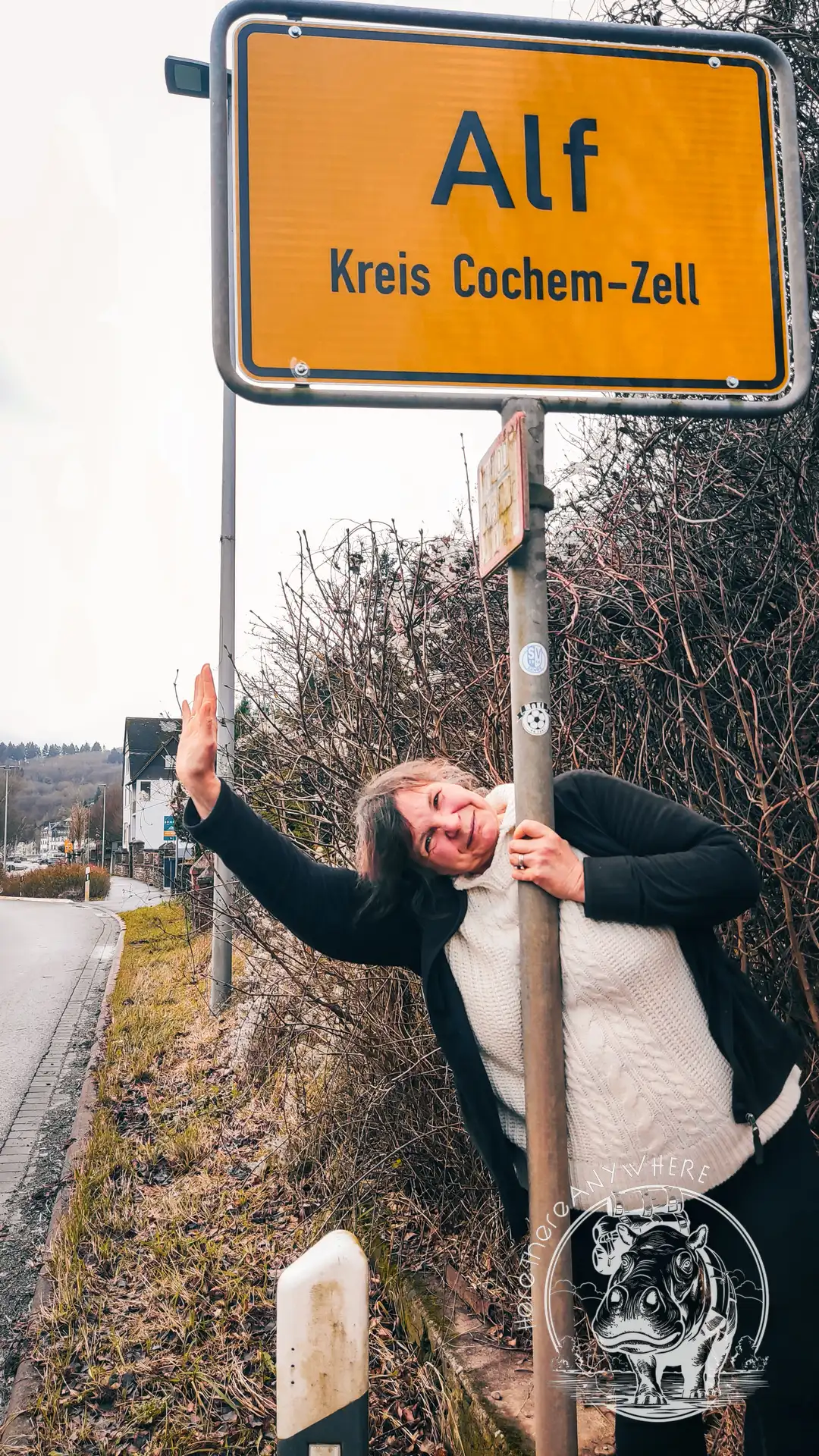 Ortschild "Alf" im Kreis Cochem-Zell / Moseltal. Tanja steht daneben und winkt.