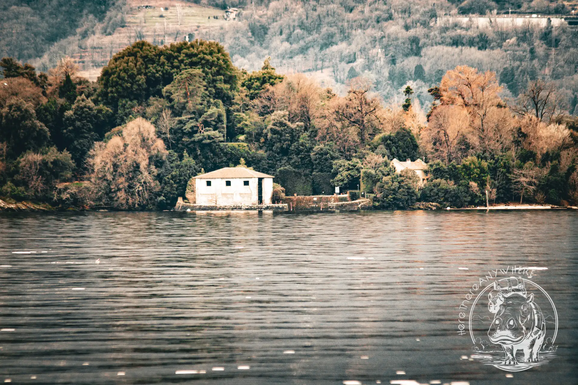 Ein See mit einem weißen Haus am gegenüberliegenden Ufer. Das Haus steht vor winterlichen Bäumen. Lago Iseo in Norditalien.